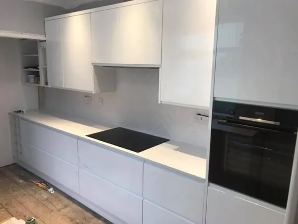 White modern kitchen with glossy cabinets, countertop, and built-in appliances.