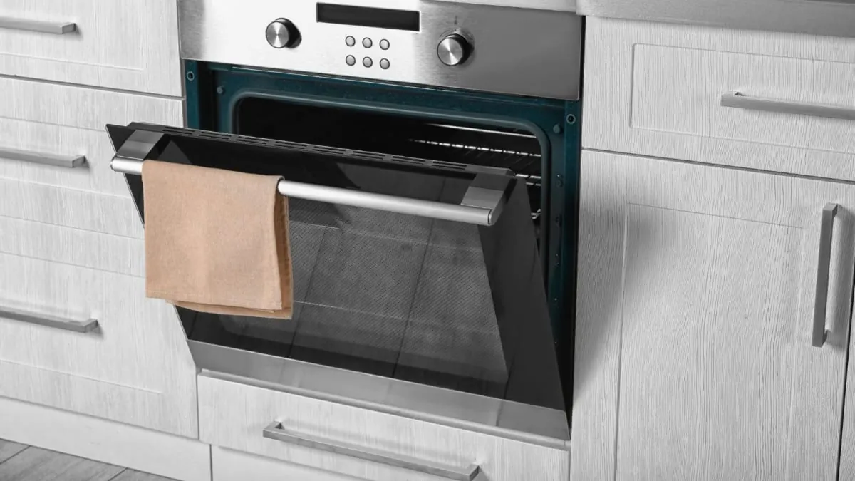 Open oven with a tan towel hanging on the handle, set in a white kitchen.