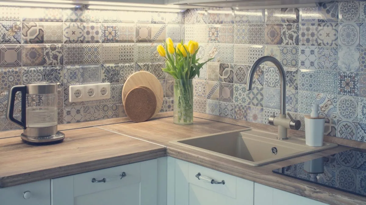 Kitchen with wooden countertops, patterned backsplash, yellow tulips, and a clear electric kettle.