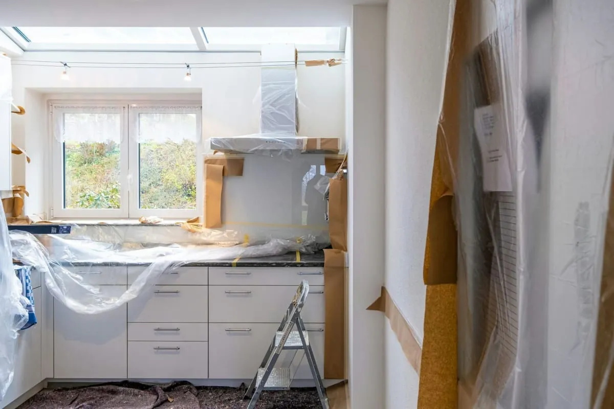 Kitchen under renovation, countertops and cabinets covered in plastic, ladder present.