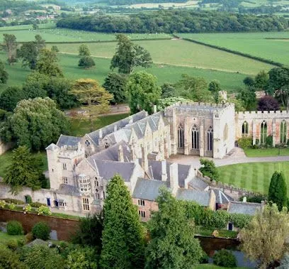 Historic stone building with multiple levels, surrounded by green trees and lawns, rural setting.