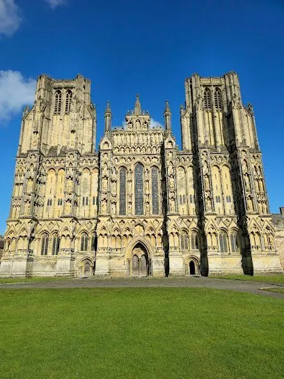 Wells Cathedral, a large stone church under a bright blue sky, on green grass.